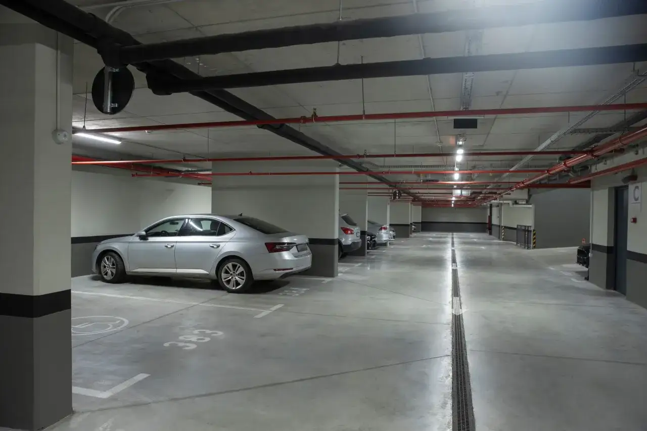 Podziemny parking w Warszawie. Zastanawiasz się, ile kosztuje miejsce parkingowe w Warszawie? Oto widok na rząd samochodów i infrastrukturę.