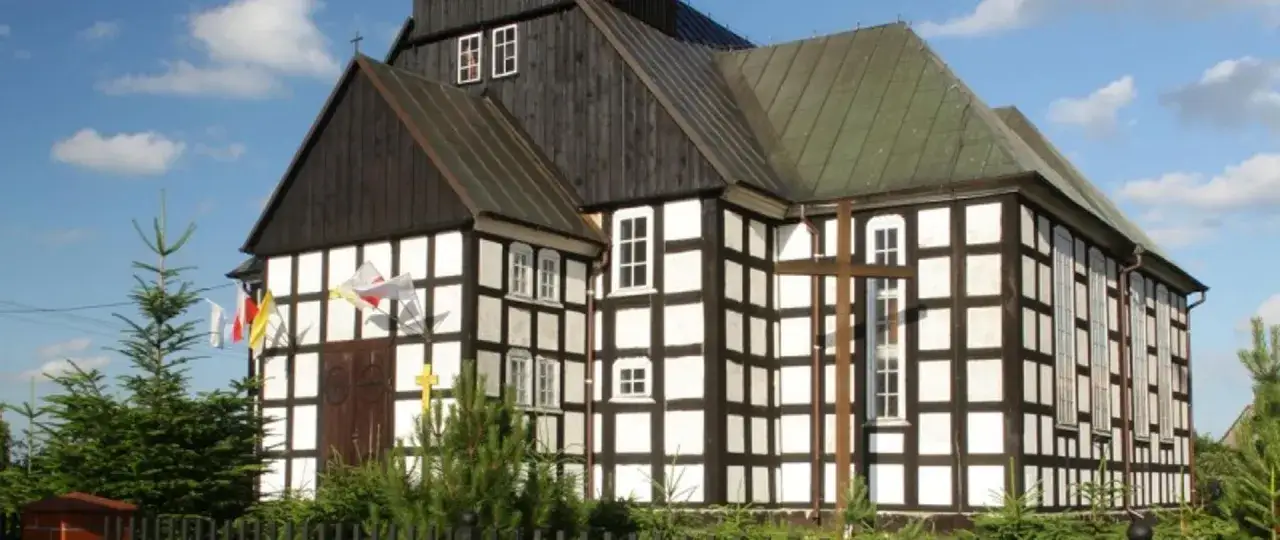 Drewniana świątynia z charakterystyczną szachownicową fasadą, kiedy dom jest zabytkiem. Krzyż przed wejściem i polskie flagi.