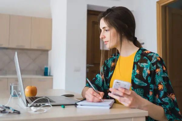 Kobieta pracuje przy laptopie, notując i sprawdzając telefon. Zastanawia się, jak obliczyć czynsz za niepełny miesiąc.